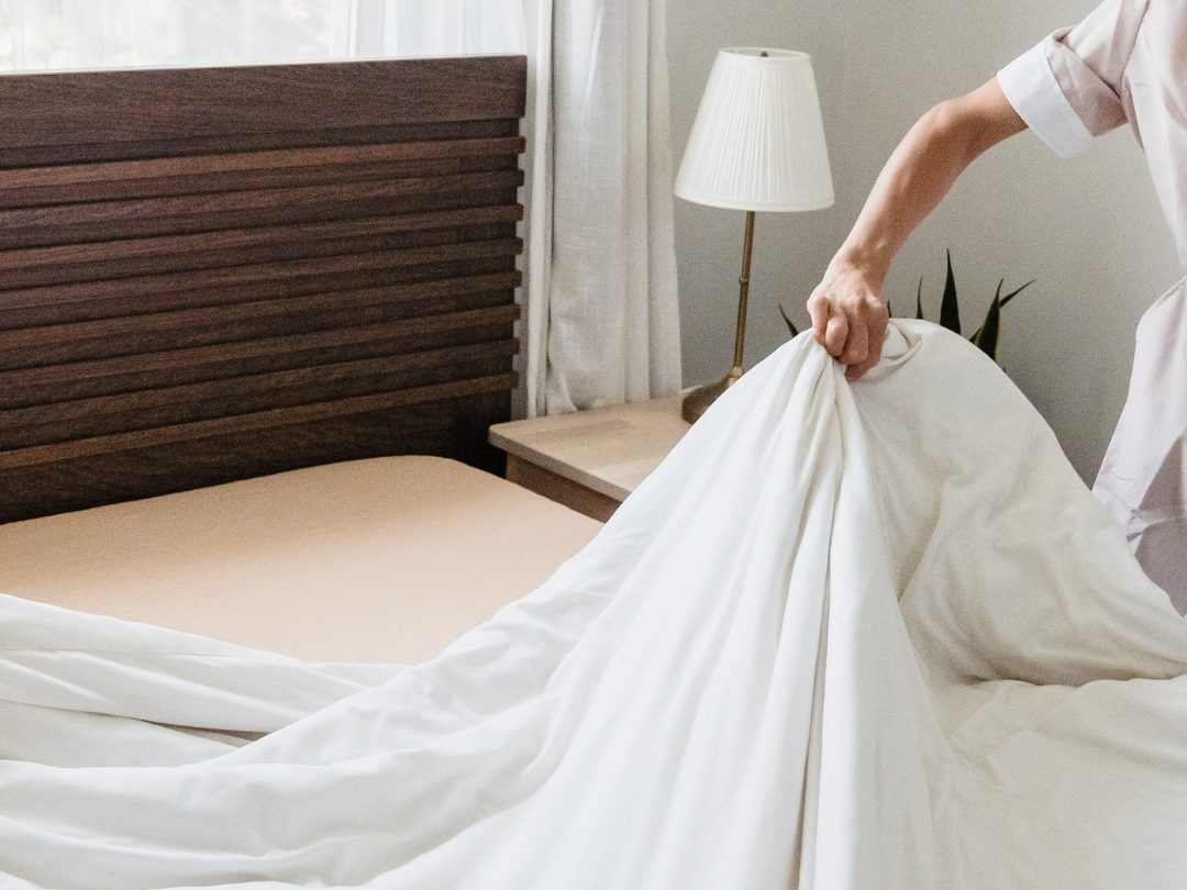 Personne tendant un drap en coton blanc sur un lit